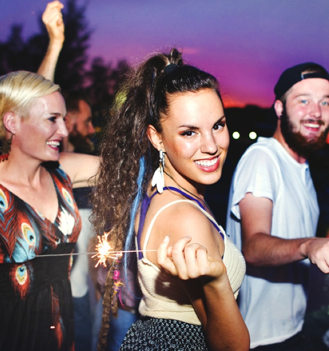 A group of young people cheerfully waving sparklers outdoors at dusk